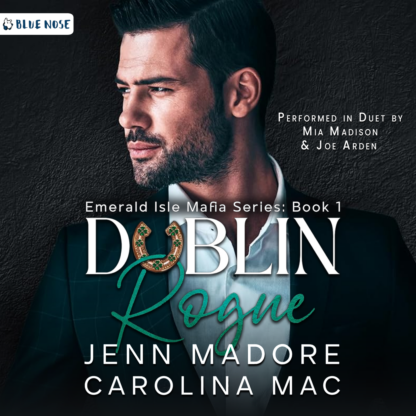 Dublin Rogue by Jenn Madore and Carolina Mac audiobook cover with a dark cement textured background and a bearded, dark-haired man in a suit looking screen left. His collar is open and he's not wearing a tie. Performed in Duet by Mia Madison and Joe Arden. Produced by Blue Nose AUDIO.